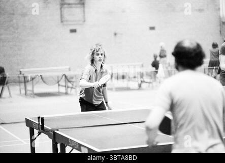 Campo da ping-pong Akersloot. Ping pong, Whizgle News, Dutch Desk, Paesi Bassi, 1950 - 2000 il 17-02-1974. Questi argomenti sono mostrati nell'immagine. In un ambiente interno spazioso, un gruppo di persone si impegna in una vivace partita a ping pong. La scena è caratterizzata da un'illuminazione soffusa e diffusa che crea un'atmosfera calda ma dinamica. Le pareti, fatte di mattoni, aggiungono una consistenza rustica, contrastando con l'elegante tavolo scuro. In primo piano, un giovane giocatore con i capelli ricci è intensamente concentrato, pronto a colpire la palla con una pagaia. La sua espressione riflette la concentrazione e la determinazione, Foto Stock
