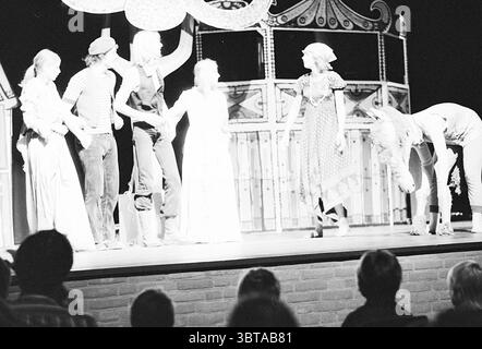 Spettacolo teatrale., Whizgle News, Dutch Desk, Paesi Bassi, 1950 - 2000. Questi argomenti sono mostrati nell'immagine. La scena raffigura uno spettacolo teatrale su un palcoscenico rialzato, caratterizzato da uno sfondo stravagante e leggermente fantastico. L'ambientazione include decorazioni ornamentali che ricordano una fiera o un carnevale, con motivi circolari e colori vivaci che suggeriscono un'atmosfera vivace, anche in tonalità monocromatiche. Un gruppo di sei artisti occupa il palco, tutti in vari costumi che suggeriscono personaggi diversi, portando un senso di narrazione alla performance. Il loro abbigliamento varia da Foto Stock