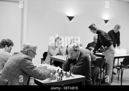 Club di scacchi nella Chiesa riformata Heemstede Heemstede Paesi Bassi, Whizgle News, Dutch Desk, Paesi Bassi, 1950 - 2000 il 04-10-1992. L'immagine mostra questi argomenti. La scena cattura un vivace torneo di scacchi al coperto. Diversi tavoli sono disposti in una sala spaziosa e luminosa, ognuno occupato da gruppi di individui coinvolti in intense partite. Le pareti sono dipinte in un colore delicato e neutro, esaltando la luminosa illuminazione sopraelevata che crea un'atmosfera calda e invitante. In prima linea, due anziani si appoggiano da vicino su una scacchiera, le loro espressioni concentrate mostrano un mix di Foto Stock