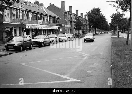 Panoramica Planetenweg IJmuiden Paesi Bassi, Whizgle News, Dutch Desk, Paesi Bassi, 1950 - 2000 il 09-09-1990. L'immagine contiene questi argomenti. La scena cattura una tranquilla strada urbana fiancheggiata da veicoli, prevalentemente piccole auto parcheggiate ordinatamente lungo il marciapiede. L'architettura presenta edifici da due a tre piani, che mostrano un mix di elementi residenziali e commerciali, con alcuni balconi adornati da semplici ringhiere. La tavolozza dei colori si inclina verso la scala dei grigi, trasmettendo un'atmosfera soffusa e quasi nostalgica. Gli edifici presentano un design tradizionale, con facciate in mattoni e grandi finestre, Foto Stock