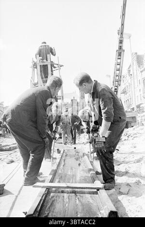 La statua di Laurens Janszoon Coster è stata progettata dallo scultore Louis Royer. La statua ha cambiato diverse volte posizione nel corso degli anni, l'ultima nel 1966. Haarlem Grote Markt Nederland., Whizgle News, Dutch Desk, Paesi Bassi, 1950 - 2000. Questi sono gli argomenti nell'immagine. La scena cattura un vivace cantiere sotto un cielo chiaro e limpido. La luce del sole proietta ombre nitide sul terreno, illuminando vari elementi in vista. Un gruppo di lavoratori è attivamente impegnato nei propri compiti, dimostrando un senso di lavoro di squadra e concentrazione. La maggior parte degli individui sono rivestiti di coaguli di lavoro scuri Foto Stock