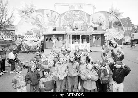 Fair, Whizgle News, Dutch Desk, Paesi Bassi, 1950 - 2000 il 04-1986. Questi argomenti sono mostrati nell'immagine. Nella scena, una grande attrazione carnevalesca domina lo sfondo, con vivaci murales adornati da motivi dinamici e stravaganti di veicoli e personaggi fantastici, tutti pieni di energia giocosa. Questo sfondo è incorniciato da due grandi strutture circolari che accentuano l'atmosfera festosa. Un gruppo di bambini, circa trenta in numero, si trova in primo piano. Sono vestiti con giacche casual, alcune con cappuccio, che riflettono il clima fresco, il tutto trasudato da un tocco di palpabile Foto Stock