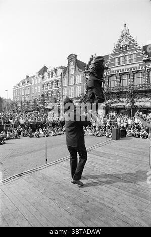 Driehuis Haarlem Bloemendaal Festival festività e manifestazioni Haarlem Paesi Bassi, Whizgle News, Dutch Desk, Paesi Bassi, 1950 - 2000 il 05-09-1973. L'immagine contiene questi argomenti. La scena cattura un vivace spettacolo all'aperto in una vivace piazza della città. In primo piano, un performer vestito con una tuta nera solleva un'altra persona in aria, mostrando un momento di esuberanza e abilità. L'individuo sollevato indossa abiti più leggeri, sottolineando il movimento sullo sfondo più scuro. Intorno a loro c'è un raduno di spettatori seduti a terra, formando un semi-cir Foto Stock