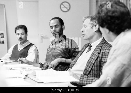 Migrants Meeting Haarlem Paesi Bassi, Whizgle News, Dutch Desk, Paesi Bassi, 1950 - 2000 il 04-11-1991. Questi argomenti sono mostrati nell'immagine. In una sala conferenze ben illuminata, quattro uomini sono impegnati in una discussione intorno a un tavolo rettangolare. L'ambiente suggerisce un ambiente professionale o accademico, caratterizzato da pareti luminose che riflettono l'illuminazione soffusa dell'ambiente. Un uomo, seduto a sinistra, ha i capelli scuri e i baffi ben curati, indossando un maglione di colore chiaro sopra una camicia con colletto. La sua postura è attenta, suggerendo che sta ascoltando attivamente. Oltre a lui, un altro uomo ha un serio ex Foto Stock