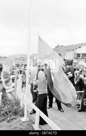 Apertura apertura apertura Zandvoortmeeuwen club Youth building calcio Zandvoortse Meeuwen Halfweg apertura apertura, Whizgle News, Dutch Desk, Paesi Bassi, 1950 - 2000 il 28-09-1974. Questi argomenti vengono visualizzati nell'immagine. In un ambiente costiero, un gruppo di persone si riunisce intorno a un palo, dove sembra che si stia svolgendo una cerimonia. L'atmosfera è di attesa e significato, con un mix di solennità ed eccitazione tra i partecipanti. A sinistra, un bambino è in primo piano, che si alza mentre aiuta a alzare una grande bandiera accanto a un adulto, che è concentrato sul compito che sta svolgendo. Quello degli adulti Foto Stock