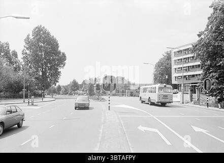 Panoramica dell'incrocio Zuiderhoutlaan - Churchillaan Overviews Haarlem Churchilllaan Paesi Bassi, Whizgle News, Dutch Desk, Paesi Bassi, 1950 - 2000 il 07-06-1973. L'immagine contiene questi argomenti. La scena raffigura un'intersezione con una disposizione circolare. In primo piano, si possono vedere due veicoli che si avvicinano alla rotonda: Un'auto di colore scuro sulla sinistra e un autobus bianco più grande che si dirige verso destra. La strada è contrassegnata da linee chiare che indicano le direzioni di svolta. Su entrambi i lati della strada, ci sono alti alberi che contribuiscono con un colore verde lussureggiante Foto Stock