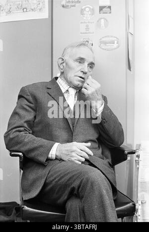 Mr. V.d. Meije Sr. Persons, Whizgle News, Dutch Desk, Paesi Bassi, 1950 - 2000 il 19-11-1974. Questi argomenti vengono visualizzati nell'immagine. In questo ambiente, un uomo anziano siede in una postura rilassata ma contemplativa, occupando una sedia scura e imbottita. È vestito con un abito grigio sartoriale formale, completato da una camicia ben pressata e da una cravatta che aggiunge un tocco di raffinatezza. La texture del vestito è ricca e suggerisce una lavorazione artigianale di qualità, mentre i motivi sottili della sua camicia creano un delicato contrasto con il tessuto solido del vestito. Il volto dell'uomo, pieno di età, mostra un mix di saggezza e truffa Foto Stock