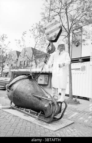 Punto più alto del pozzo a Heemstede Heemstede Nederland, Whizgle News, Dutch Desk, Paesi Bassi, 1950 - 2000 il 19-06-1991. L'immagine include questi argomenti. La scena vede un uomo in piedi con sicurezza su un grande oggetto dall'aspetto industriale che assomiglia a un pezzo fuso pesante o a un meccanismo di sollevamento. Indossa un lungo cappotto bianco, che contrasta nettamente con gli elementi circostanti. La sua espressione è di orgoglio o di divertimento, aggiungendo un senso di leggerezza all'ambiente altrimenti robusto. Sullo sfondo, ci sono modesti edifici a due piani con tetti inclinati e grandi finestre, a suggerire Foto Stock