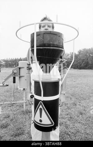 Hans Hessels jogger al palo sniffing Walking, Whizgle News, Dutch Desk, Paesi Bassi, 1950 - 2000 on 28-06-1989. Questi sono gli argomenti nell'immagine. Nella scena, un uomo si trova in un campo erboso, posizionato direttamente dietro un grande dispositivo cilindrico che domina il primo piano. Il dispositivo è dotato di una combinazione di colori in bianco e nero, con un segnale di avvertenza visibile sulla sua superficie. L'uomo è parzialmente oscurato dall'equipaggiamento, con la testa e la parte superiore del corpo che sporgono da dietro. Il suo abbigliamento appare casual, costituito da una giacca di colore chiaro sovrapposta a una camicia più scura, e lui Foto Stock