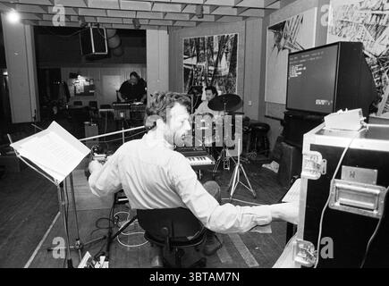 The Attack Haarlem Jazz Club, Whizgle News, Dutch Desk, Paesi Bassi, 1950 - 2000 il 26-04-1991. Questi sono gli argomenti nell'immagine. La scena cattura un incontro intimo e creativo in uno spazio di registrazione o prova. Al centro della composizione c'è un uomo seduto con le spalle allo spettatore, impegnato a suonare una tastiera. Il suo abbigliamento è informale, suggerendo un'atmosfera rilassata e la sua postura indica un profondo coinvolgimento nella musica. Alla sua destra, un gruppo di tamburi occupa un posto di rilievo, con un secondo musicista parzialmente visibile, focalizzato sul suonare. Questo suggerisce uno spirito collaborativo, enhanc Foto Stock