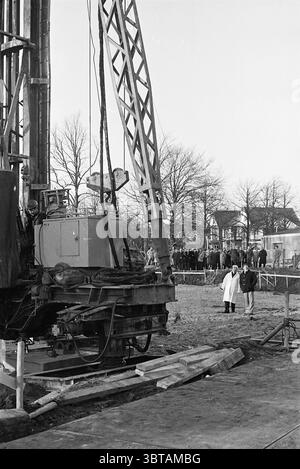 Terrazza al primo polo Beverwijk di fronte al primo polo della stazione, Whizgle News, Dutch Desk, Paesi Bassi, 1950 - 2000 su 17-12-1975. Questi sono gli elementi dell'immagine. La scena cattura un vivace cantiere sotto un cielo luminoso, illuminato dalla luce del giorno che proietta ombre delicate e mette in luce vari elementi. All'avanguardia, un grande macchinario domina lo spazio, la sua struttura metallica robusta e imponente. Il braccio della gru si estende verso l'alto, dove è pronto per sollevare materiali pesanti, mostrando dettagli meccanici complessi come cavi e pulegge. Intorno al machi Foto Stock