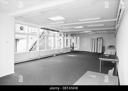 Biblioteca scolastica., Whizgle News, Dutch Desk, Paesi Bassi, 1950 - 2000 nel 1978. Questi argomenti vengono visualizzati nell'immagine. La scena raffigura una camera spaziosa e vuota caratterizzata da un'estetica minimalista. Il pavimento e' coperto da un tappeto grigio, che fornisce un delicato contrasto con le luminose pareti bianche. La luce naturale inonda l'area attraverso grandi finestre a tutta altezza che si affacciano su un lato, creando un'atmosfera luminosa e ariosa. Sopra, una griglia di apparecchi di illuminazione fluorescenti fornisce un'illuminazione aggiuntiva, migliorando delicatamente la luminosità della stanza. Il soffitto è semplice e ordinato, con vista Foto Stock