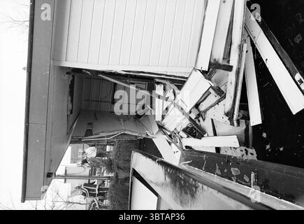 Casa galleggiante collisione Spaarne Houseboats, Whizgle News, Dutch Desk, Paesi Bassi, 1950 - 2000 il 03-02-1989. L'immagine mostra questi argomenti. La scena cattura un edificio che ha subito notevoli danni strutturali. L'esterno presenta una facciata in legno, con tavole di colore pallido scheggiate e spostate. Diverse tavole sono sparse casualmente intorno alla base, suggerendo un forte impatto. L'ingresso appare socchiuso, con pezzi di legno appesi precariamente, a indicare un disturbo. Sullo sfondo, si infila un cielo cupo, contribuendo a creare un'atmosfera ricoperta che aggiunge al sombo Foto Stock