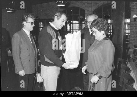 Ricevimento d'addio Mr. Blokker HD Haarlems Dagblad ecc. e IJmuider Courant e Koeri, Whizgle News, Dutch Desk, Paesi Bassi, 1950 - 2000 al 14-02-1986. L'immagine include questi argomenti. In un ambiente interno illuminato con calore, un gruppo di quattro persone sta interagendo, evocando un senso di cameratismo e celebrazione. Le pareti sono adornate con mattoni, contribuendo a creare un'atmosfera intima. Al centro, un uomo tiene in mano un regalo avvolto in carta bianca comune, che sembra presentarlo a una donna con i capelli scuri ricci. Il suo volto mostra un mix di curiosità e gioia, suggerendo che questo momento è speciale. Lei è il dottor Foto Stock