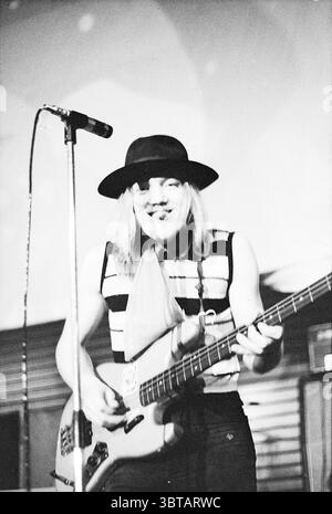 Esibizione dei Cats della Dizzy Man's Band e di altri artisti e gruppi. Music, Whizgle News, Dutch Desk, Paesi Bassi, 1950 - 2000 on 26-11-1970. Questi argomenti vengono visualizzati nell'immagine. In un'atmosfera dinamica, un musicista è in prima linea, suonando con sicurezza il basso. Sfoggia un cappello a tesa larga che gli proietta una leggera ombra sul viso, aggiungendo un'aria di mistero. I suoi capelli lunghi e fluenti donano un senso di movimento, completando l'energia vivace delle prestazioni. Il musicista indossa un top senza maniche a righe, che crea un netto contrasto con la finitura liscia e lucida dei ins Foto Stock