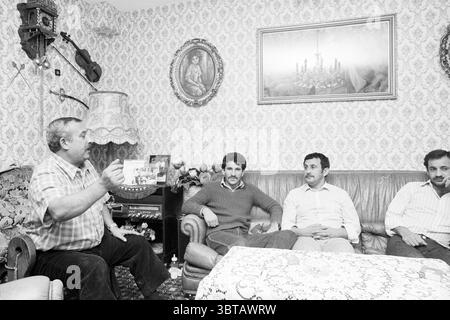 Zigeuner fam. Barjonooy Lelystad Zigeuners Lelystad, Whizgle News, Dutch Desk, Paesi Bassi, 1950 - 2000 il 02-03-1983. Questi sono gli argomenti nell'immagine. In una camera decorata con calore, quattro uomini sono riuniti, seduti comodamente su un morbido divano in pelle invecchiata. L'atmosfera trasuda un senso di cameratismo e nostalgia. Le pareti sono adornate da intricate tappezzerie floreali, caratterizzate da sfumature di crema e giallo tenue, che aggiungono un delicato fascino vintage all'ambiente. L'illuminazione è soffusa, emettendo un caldo bagliore che si mescola con i toni terrosi della tappezzeria e dell'arredamento. Un delicato tavolo in pizzo Foto Stock