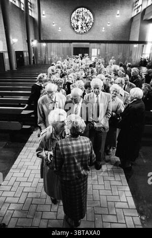 40 anni. Anniversario Sister IJmuiden IJmuiden Paesi Bassi, Whizgle News, Dutch Desk, Paesi Bassi, 1950 - 2000 il 19-10-1991. L'immagine contiene questi argomenti. La scena si sviluppa all'interno di uno spazioso ambiente interno che ricorda un luogo di culto o di riunione della comunità, caratterizzato da alti soffitti e grandi finestre che consentono di filtrare la luce soffusa e diffusa. Una vetrata circolare domina un'estremità, caratterizzata da intricati disegni che proiettano riflessi colorati sulle sfumature delle pareti circostanti. Una folla di individui per lo più anziani occupa la navata centrale, d Foto Stock