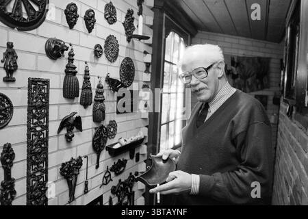 Architetto van den Akker Zwanenburg Zwanenburg, Whizgle News, Dutch Desk, Paesi Bassi, 1950 - 2000 il 20-02-1991. Questi argomenti vengono visualizzati nell'immagine. La scena raffigura un signore anziano in una calda e invitante stanza piena di una serie di oggetti decorativi. Si erge vicino a un muro adornato da una eclettica collezione di ornamenti e sculture in metallo, che mostra dettagli intricati e texture diverse, creando un arazzo artistico visivamente ricco. Gli oggetti includono varie forme e figure, da uccelli e fiori a disegni astratti, tutti che gettano sottili ombre sulla parete di mattoni di colore chiaro. Foto Stock