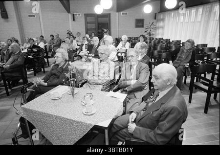 Choir Haarlemmer oil in Church Fidelishof Koren, Whizgle News, Dutch Desk, Paesi Bassi, 1950 - 2000 il 09-11-1987. L'immagine mostra questi argomenti. La scena si sviluppa in una spaziosa sala piena di file di sedie, dove un raduno di persone anziane si siede tranquillamente. L'illuminazione è morbida e calda, emessa dalle luci a sospensione rotonde che pendono dall'alto soffitto, emettendo una luce soffusa sulla stanza. Seduti in file ordinate, i partecipanti mostrano una varietà di espressioni, alcune attente, altre contemplative o leggermente inquiete. L'abbigliamento riflette una vasta gamma di stili, con molti o Foto Stock