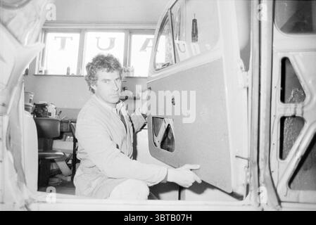 Azienda di assemblaggio porte auto garage, Whizgle News, Dutch Desk, Paesi Bassi, 1950 - 2000 il 23-04-1986. Questi argomenti vengono visualizzati nell'immagine. La scena si sviluppa in un'officina, illuminata da una luce soffusa e diffusa che crea un'atmosfera calda e invitante. Lo spazio è pieno di strumenti e attrezzature tipici di un'officina di riparazione auto, che suggeriscono attività e senso dello scopo. Un uomo è posizionato in primo piano, concentrato sul suo compito. Ha i capelli ricci e un'espressione seria, che indica la concentrazione. È vestito con una giacca da lavoro di colore chiaro, che contrasta leggermente con la Foto Stock