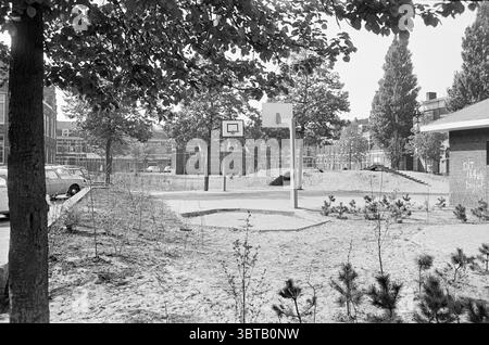 Panoramica Leidscheplein Haarlem Overviews Square Haarlem Leidseplein Paesi Bassi, Whizgle News, Dutch Desk, Paesi Bassi, 1950 - 2000 il 18-05-1976. L'immagine include questi argomenti. La scena raffigura una tranquilla area esterna, caratterizzata da una miscela di elementi naturali e urbani. In primo piano, un campo da basket rettangolare è caratterizzato da una superficie liscia e sabbiosa, con il suo cerchio ben visibile sullo sfondo di alberi ed edifici. A sinistra, il robusto tronco di un albero si erge a sentinella, che lascia un verde vibrante in contrasto con i toni tenui del terreno sabbioso, il che suggerisce un Foto Stock
