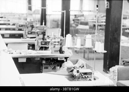 Laboratorio di cucito illegale Halfweg Halfweg, Whizgle News, Dutch Desk, Paesi Bassi, 1950 - 2000 il 10-05-1993. L'immagine include questi argomenti. La scena cattura un ampio spazio di lavoro industriale dedicato alla cucitura e alla produzione di tessuti. L'impostazione è caratterizzata da una serie di tavoli lunghi, ciascuno rivestito di varie macchine da cucire e utensili. Le macchine sono di stili diversi, alcuni vintage, che accennano a una lunga tradizione artigianale, mentre altri appaiono più moderni. La tavolozza dei colori è prevalentemente silenziata, con sfumature di grigio e bianco sporco che dominano la scena, conferendo un po' cupo Foto Stock