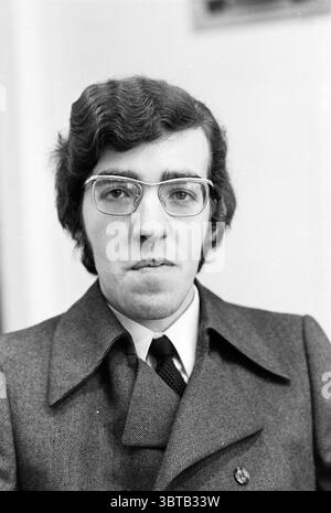 Staff + interno Uddeholm Uddeholm NV, Whizgle News, Dutch Desk, Paesi Bassi, 1950 - 2000 il 18-02-1971. L'immagine mostra questi argomenti. La scena presenta un ritratto di un giovane uomo con un'espressione seria, incorniciato in una vista ravvicinata. Ha capelli scuri e spessi, acconciati in modo leggermente ondulato, che cadono appena sopra le orecchie. I suoi occhiali hanno una forma geometrica distintiva, che aggiunge al suo aspetto intellettuale. L'uomo è vestito con un elegante cappotto grigio, sartoriale e strutturato, che sfoggia un look classico. Sotto, è visibile una camicia bianca, insieme a una cravatta scura che ci armonizza Foto Stock