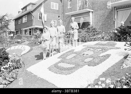 Flower Girls in Volendam Flowers and Flower Girls, Whizgle News, Dutch Desk, Paesi Bassi, 1950 - 2000 il 27-04-1968. Questi argomenti vengono visualizzati nell'immagine. In un incantevole giardino, quattro donne stanno insieme, ognuna rivestita in eleganti abiti dai colori chiari che irradiano un senso di unità e stile. Le loro espressioni sono luminose e accoglienti, contribuendo ad un'atmosfera complessivamente allegra. Ogni donna ha in mano un piccolo cesto decorato con fiori, che esalta l'atmosfera festosa della scena. Il giardino stesso e' meticolosamente disposto, caratterizzato da una variegata gamma di fiori e piante che suggeriscono un Foto Stock