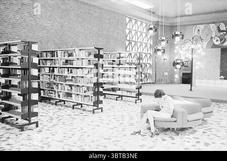Interno di una biblioteca., Whizgle News, Dutch Desk, Paesi Bassi, 1950 - 2000. Questi sono gli elementi dell'immagine. La scena è ambientata in una spaziosa biblioteca caratterizzata da uno stile architettonico moderno. Le pareti sono fatte di mattoni rossi a vista, donando alla camera un'atmosfera calda ma industriale. A sinistra, alte librerie piene di libri si estendono verso l'alto, i loro scaffali sono organizzati in righe ordinate, creando un senso di ordine e ricerca intellettuale. Al contrario, il pavimento è un mosaico di piastrelle chiare e scure, che conferisce texture allo spazio con la sua disposizione irregolare. L'illuminazione è luminosa ma morbida, e. Foto Stock
