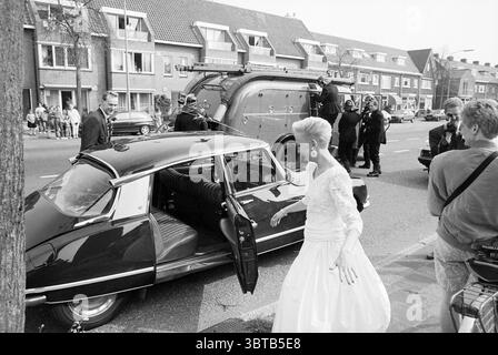 Matrimonio presso i vigili del fuoco Haarlem Paesi Bassi, Whizgle News, Dutch Desk, Paesi Bassi, 1950 - 2000 il 09-04-1992. Questi sono gli argomenti nell'immagine. La scena si snoda su una vivace strada urbana, incorniciata da una fila di edifici pittoreschi che mostrano un mix di architettura moderna e tradizionale. Il marciapiede è fiancheggiato da spettatori, che variano sottilmente in età e abbigliamento, alcuni impegnati in conversazione mentre altri guardano intensamente con espressioni curiose. In primo piano, un'elegante auto d'epoca nera spicca in primo piano, con la superficie lucida che riflette l'attività circostante. La porta dell'auto è spaventa Foto Stock