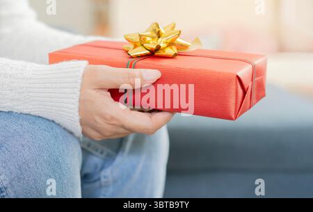 Immagine ravvicinata di una donna anziana seduta sul divano e che regge un regalo di Natale. Celebra il concetto di regalo. Foto Stock