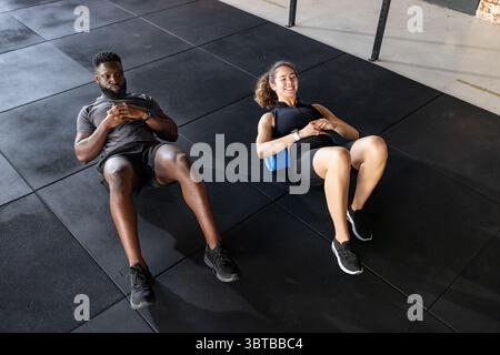 Diversi partner di allenamento sdraiati su rulli in schiuma nell'abbigliamento sportivo che si allenano in palestra con smartwatch Foto Stock