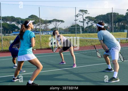 Diversi gruppi di tennisti in piedi pronti sul campo all'aperto, tenendo le racchette vicino alla rete Foto Stock