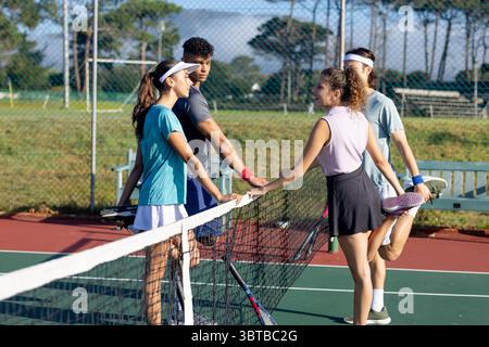 Diversi tennisti in abbigliamento sportivo che si appoggiano su una rete sul campo del parco tenendo racchette e chiacchierando Foto Stock