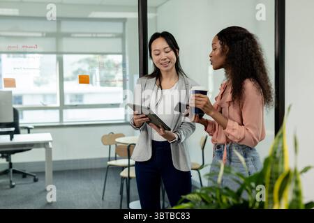 Diversi colleghi che esaminano le note della partizione in vetro in ufficio con tablet e tazze da caffè, spazio per le copie Foto Stock