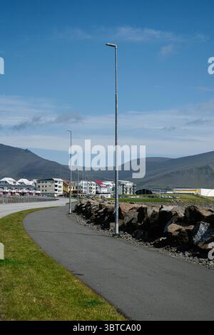 Sentiero lastricato ad Akranes, Islanda, fiancheggiato da lampioni vicino a edifici residenziali e montagne. Foto Stock