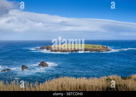 Piccola isola vulcanica circondata dalle profonde acque blu dell'Oceano Atlantico a Ponta topo, Sao Jorge, con il suggestivo cielo nuvoloso. Isolotto remoto, scogliere costiere, Foto Stock