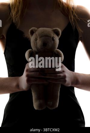 Una donna con un vestito nero tiene in mano un orsacchiotto. Foto Stock