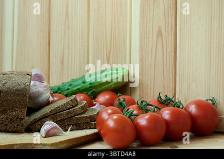 Pane assortito, pomodori e cetrioli disposti su un tagliere di legno. Foto Stock