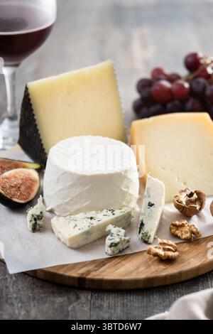Tagliere di formaggi diversi con noci, fichi e uva su tavola di legno Foto Stock