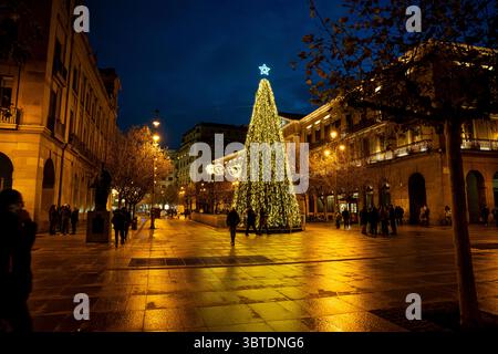 I visitatori passeggiano per le affascinanti strade di Pamplona, godendosi una serata festosa illuminata da un grande albero di Natale adornato di luci e a s. Foto Stock