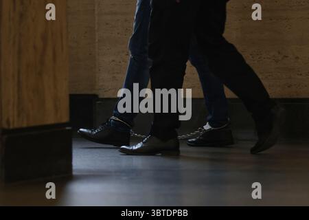 Un uomo arrestato con le manette alle gambe viene scortato in tribunale. Foto illustrativa. Foto Stock