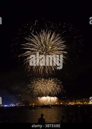 Brillanti fuochi d'artificio che esplodono sull'acqua illuminando san sebastián di notte durante la celebrazione della semana grande Foto Stock