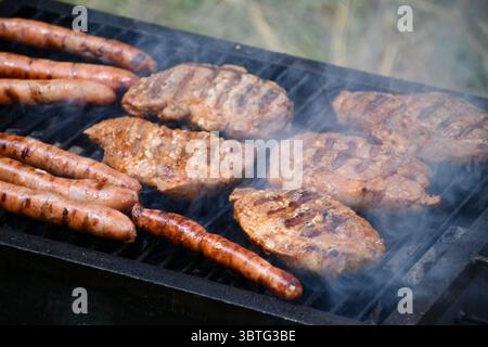 Salsicce assortite e succose bistecche di maiale cucinate su un grill caldo per fumatori all'aperto Foto Stock