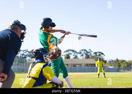 Diversi giocatori di baseball in uniformi verdi e gialle che fanno oscillare la mazza metallica sulla palla bianca sul campo Foto Stock