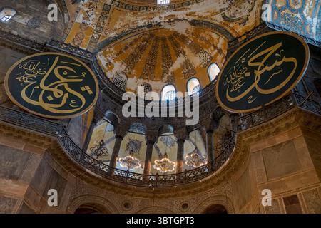 Un grande medaglione di calligrafia islamica verde e oro è appeso sotto la cupola ornata all'interno della storica Moschea di Santa Sofia a Istanbul, Turchia. Foto Stock