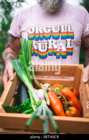 Agricoltore che mostra con orgoglio una cassa di legno piena di una varietà di verdure appena raccolte, mostrando la taglia della sua fattoria Foto Stock