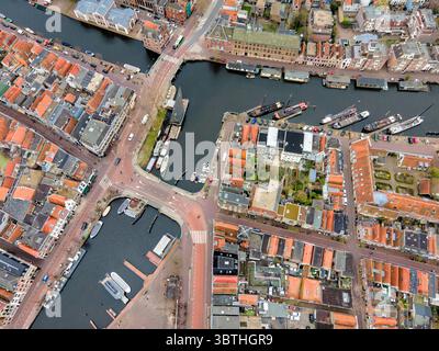 La vista aerea dei tetti in terracotta incontra le acque scure dei canali fiancheggiati da barche, un vivace arazzo nel cuore della città, Almere, Flevoland, Paesi Bassi. Foto Stock