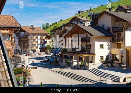Tradizionali case di villeggiatura alpina con balconi in legno incastonate nelle verdi colline di San Cassiano, Dolomiti, sotto un cielo azzurro e limpido. Foto Stock