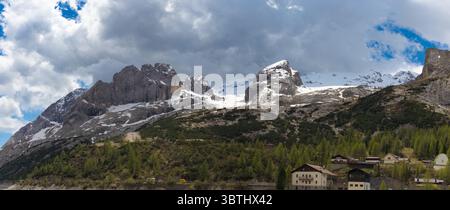 Vista panoramica delle maestose cime innevate della Marmolada che torreggiano su un lussureggiante paesaggio verde con case alpine sparse nelle Dolomiti. Foto Stock